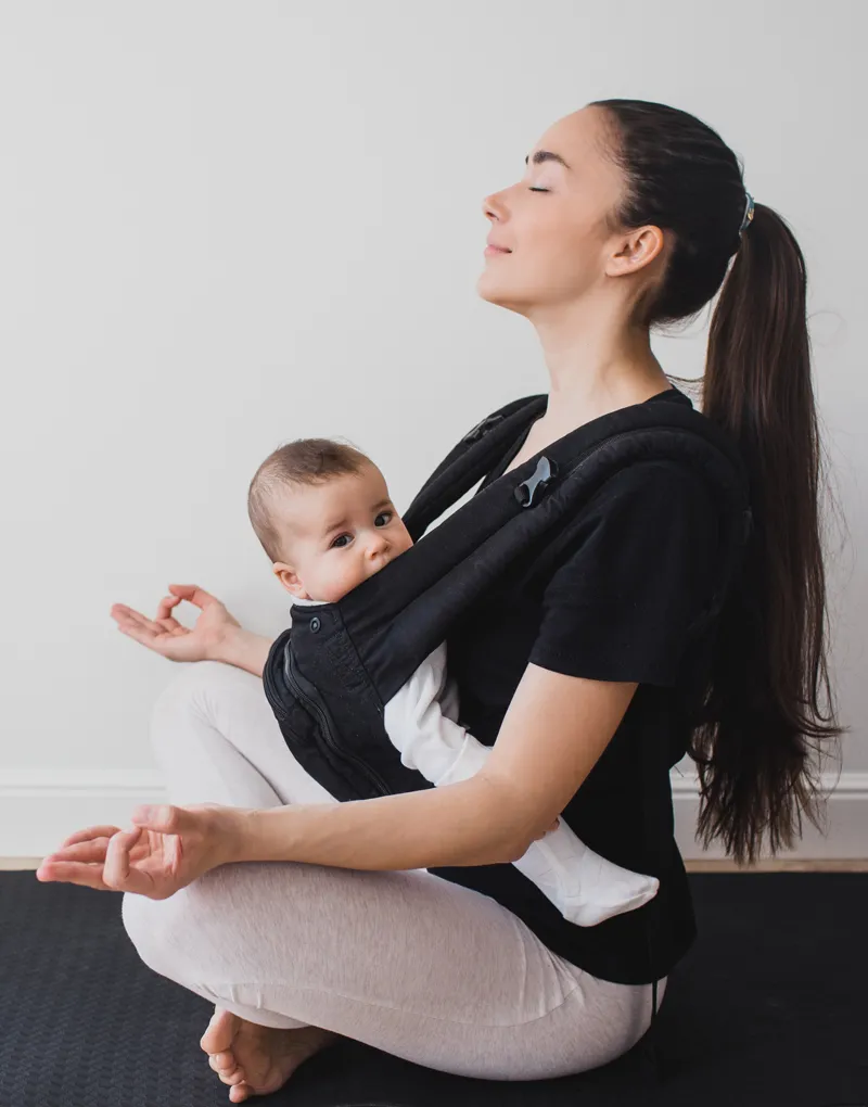 A mother sitting in meditation with her infant in a carrier